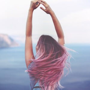 Woman with pink hair standing on the mountain top over blue sea view, photo toned