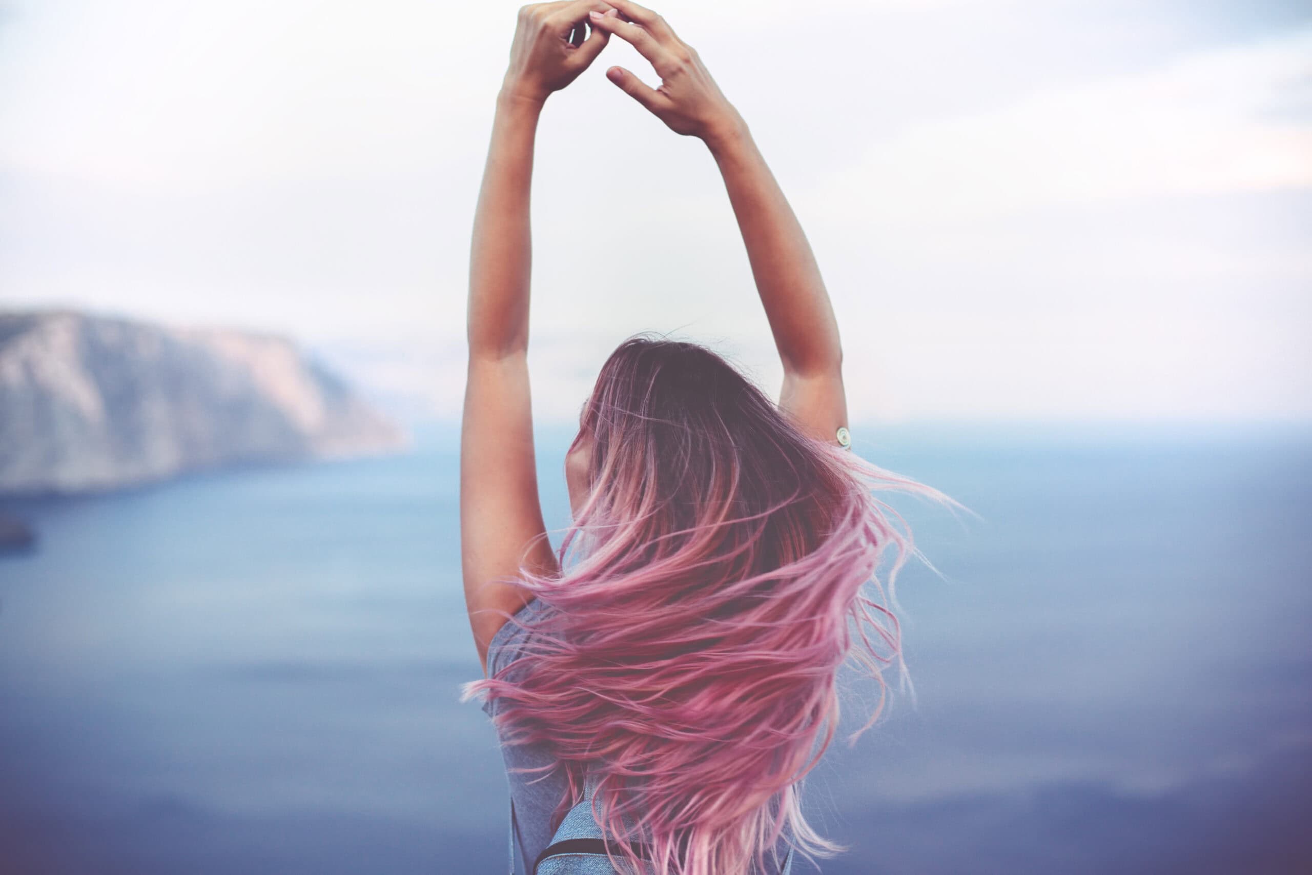 Woman with pink hair standing on the mountain top over blue sea view, photo toned