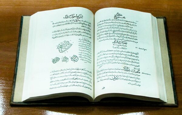 The Canon of Medicine opened to a center page, sitting on a wooden desk or table.