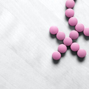 Pink birth control pills are lined up in the shape of the a woman's symbol, on a gray background. Medicine for woman. Menopause, pms, menstruation or estrogen concept. Female health. Gender symbol made from pink red pills or tablets on wooden table.