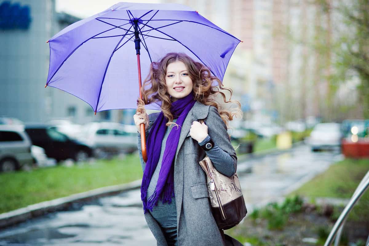 Portrait of pregnant woman with umbrella in the rain, grey coat, long reddish curly hair.