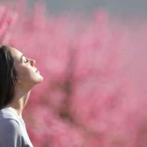 Profile of a relaxed woman breathing fresh air in a pink field of peach trees. Mental health and contraception options.