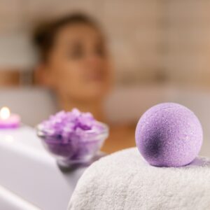Woman in bathtub healthcare self-care with purple bathbomb and candles.