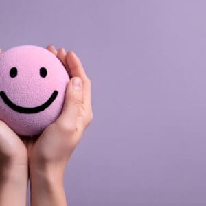 Holding a head with a happy smiling face in the hands, mental health concept, positive thinking, support and evaluation. Purple color of Caya Diaphragm
