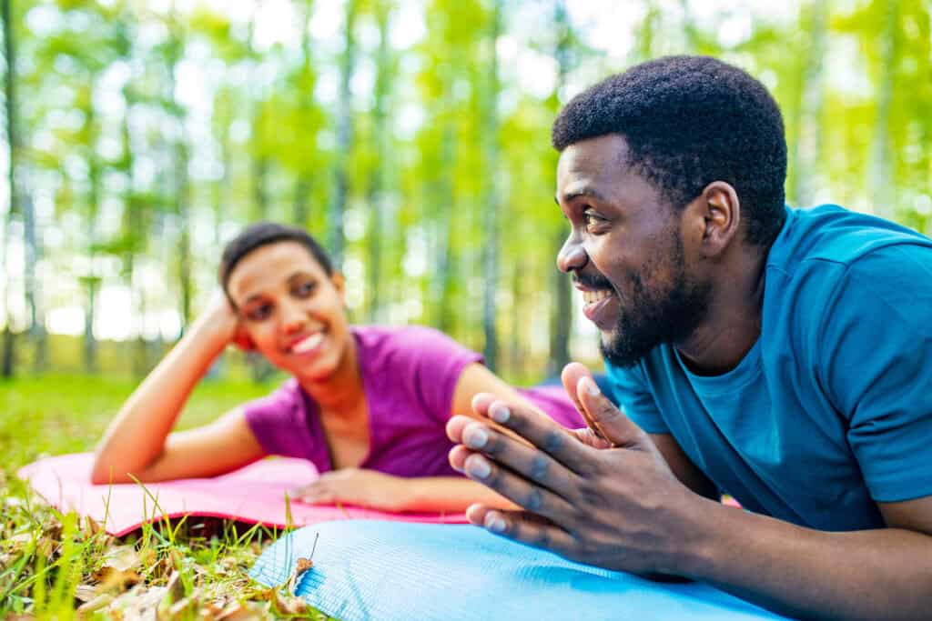 Mixed race couple lounging on yoga mats outdoors, talking and smiling.