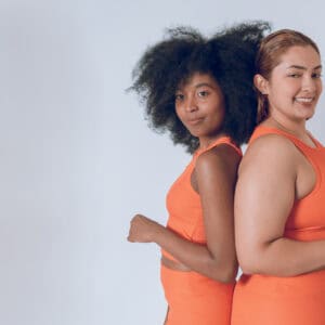 multiethnic beautiful young hispanic latina girls, posing with their backs together, looking at camera, wearing orange sportswear on a white background. image with copy space.