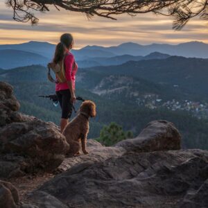 A hispanic woman is hiking with a dog, at sunset, in the Rocky Mountains near Denver, Colorado, USA