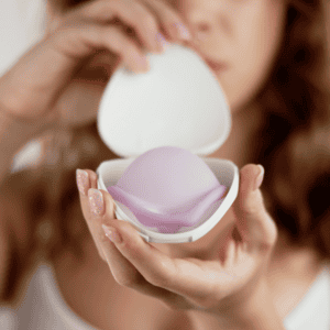 A young woman with long hair holding up a silicone Caya diaphragm that is sitting inside the opened clamshell case.